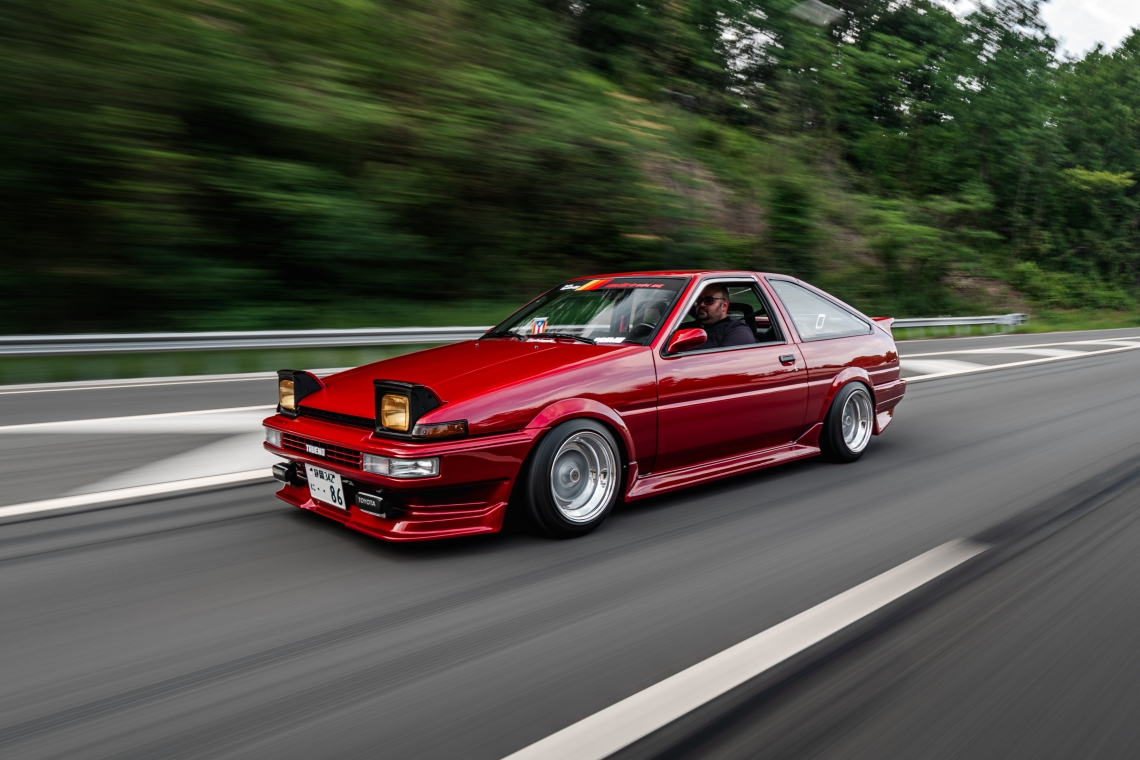 Red Toyota AE86 rolling shot on road with lowered stance and SSR MKII wheels