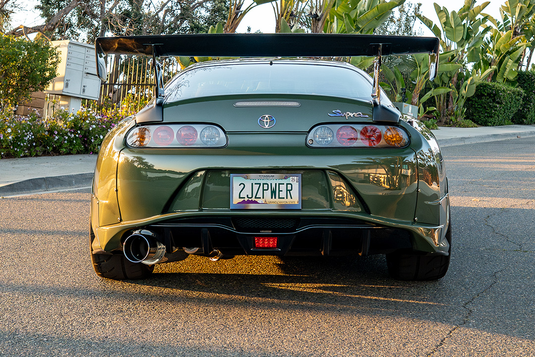 Rear view of Leopold Barrit’s 1995 Toyota Supra featuring a Varis GT wing, diffuser, and Military Olive Green finish at sunset.