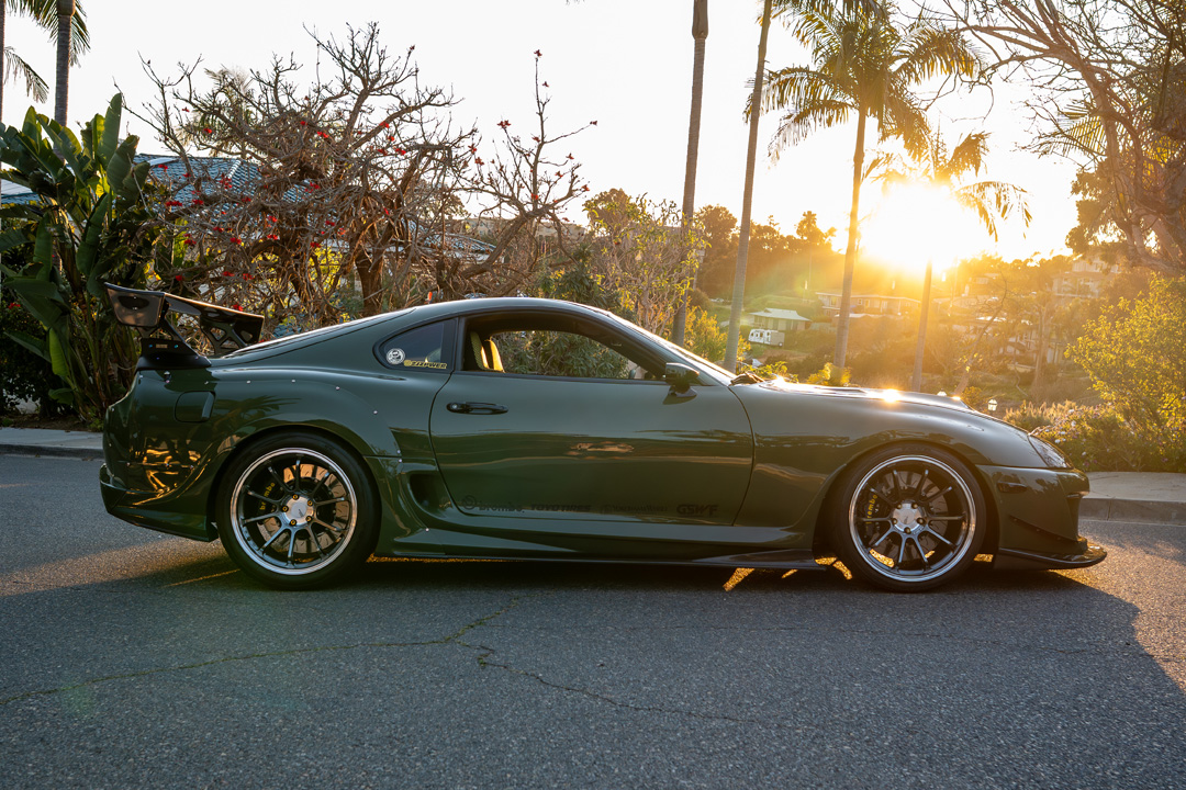 Side profile of Leopold Barrit’s Military Olive Green 1995 Toyota Supra parked at sunset with Varis widebody aero and Advan wheels.