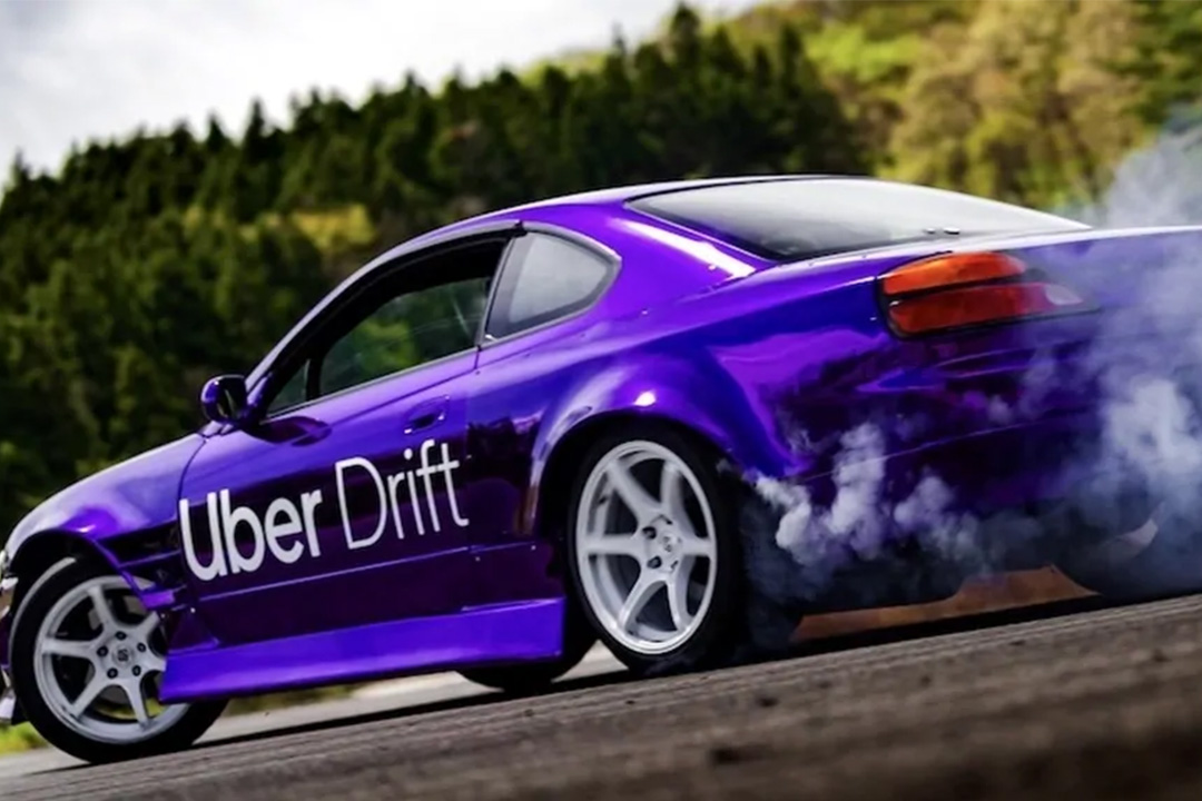 Purple Nissan Silvia S15 drift car with Uber Drift branding sliding on track outside Tokyo.