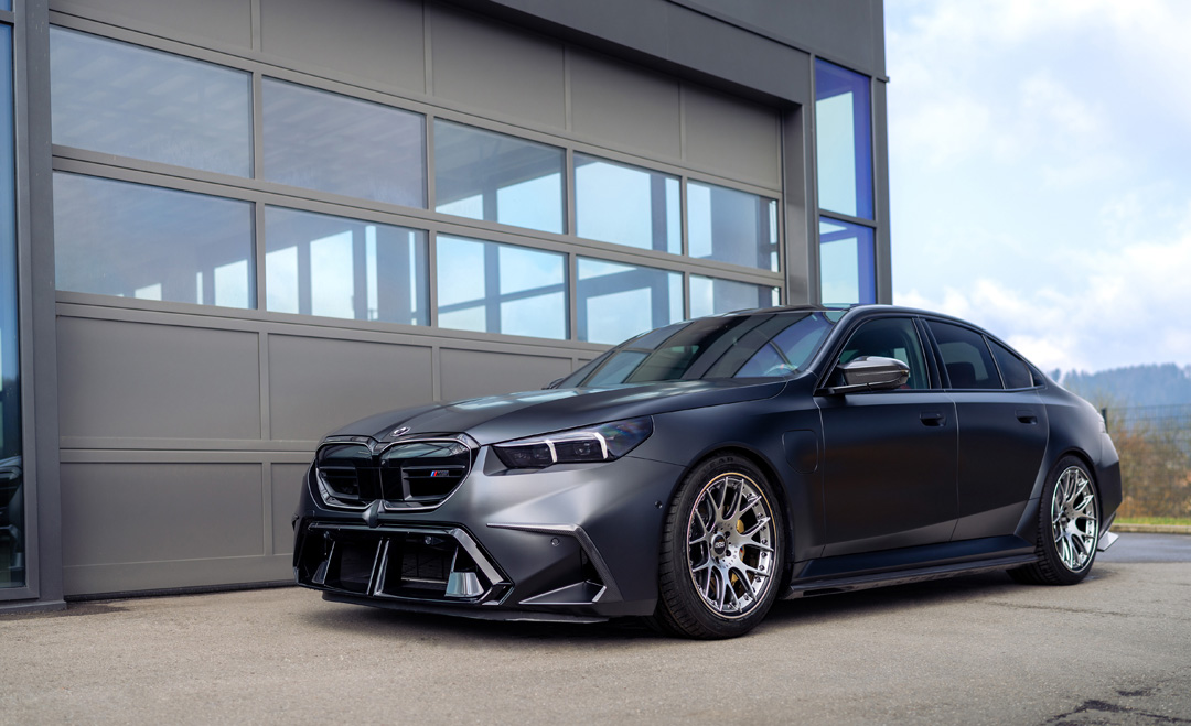 BMW M5 G90 Sedan lowered on KW springs, shown from the front three-quarter angle outside a garage.