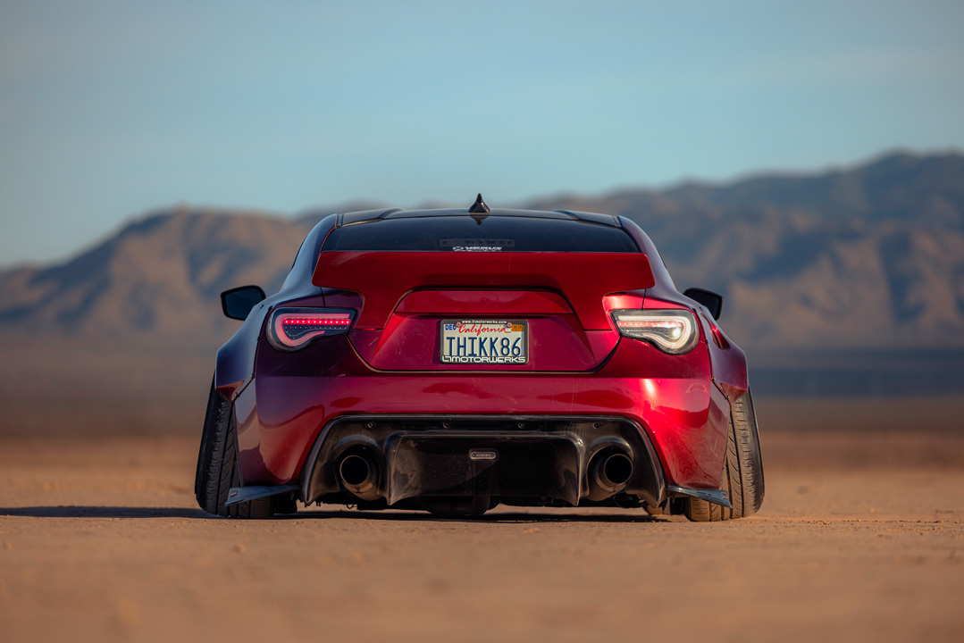 Rear view of Anthony Gonzales’ red widebody Scion FR-S parked in the desert with mountains in the background.