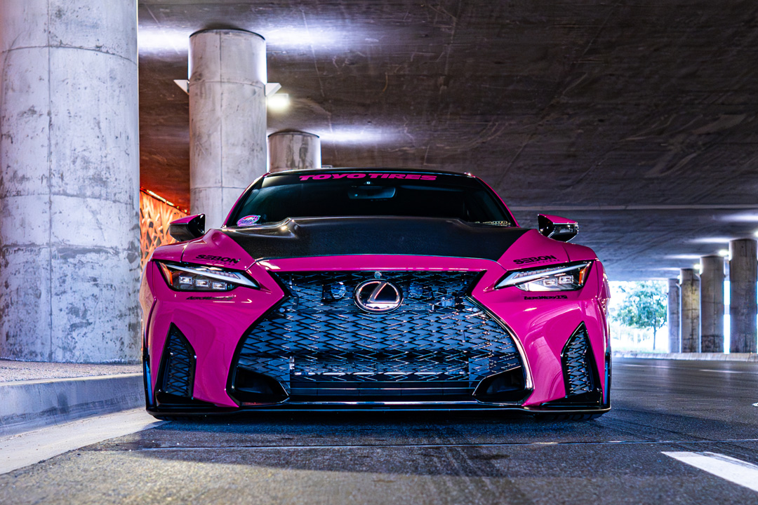 Front view of Giuseppe Balthasar’s pink widebody Lexus IS 500 parked under a concrete overpass.