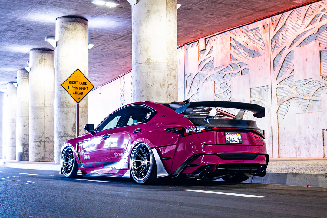 Rear three-quarter view of Giuseppe Balthasar’s pink widebody Lexus IS 500 under a lit concrete overpass.