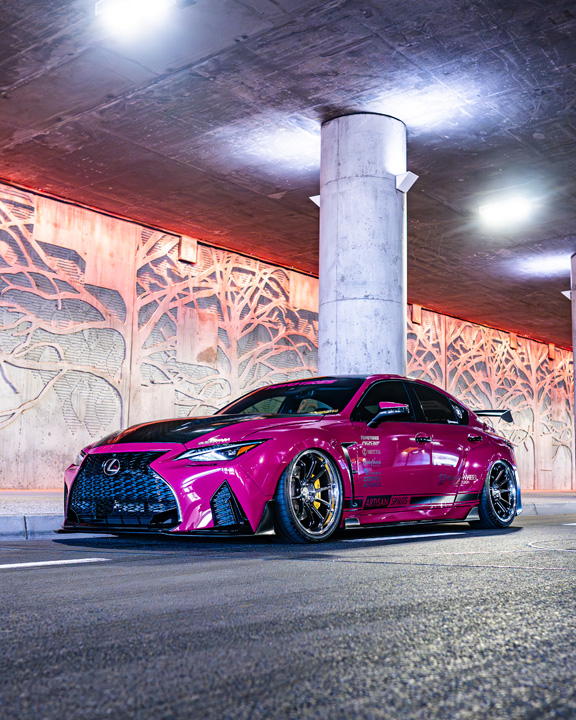 Front three-quarter view of Giuseppe Balthasar’s pink widebody Lexus IS 500 under a lit concrete overpass.
