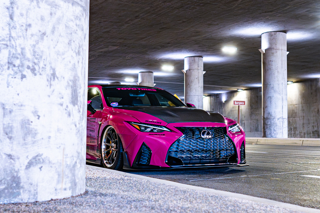 Front three-quarter view of Giuseppe Balthasar’s pink widebody Lexus IS 500 partially framed by a concrete pillar.