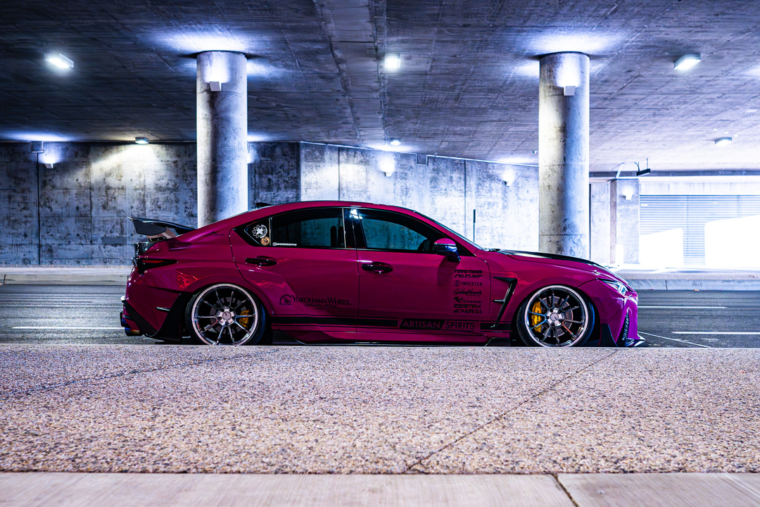 Full side profile of Giuseppe Balthasar’s pink widebody Lexus IS 500 under a lit concrete overpass.