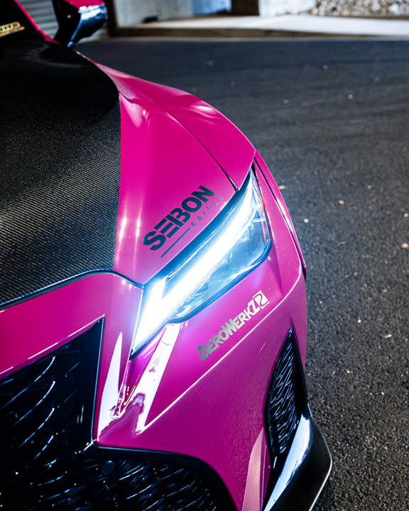 Close-up of the headlight, Seibon carbon hood, and Aerowerkz decal on Giuseppe Balthasar’s pink Lexus IS 500.