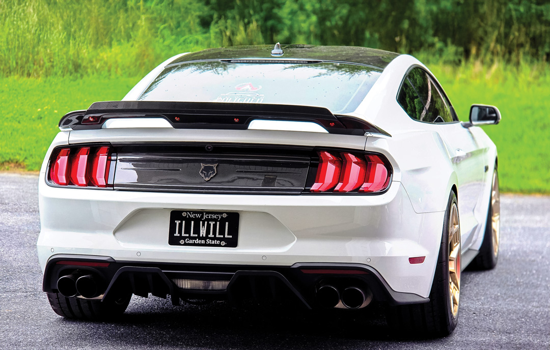 Rear three-quarter view of William Howard's white 2018 Ford Mustang GT showing the carbon deck lid, spoiler, quad exhaust, and gold wheels.
