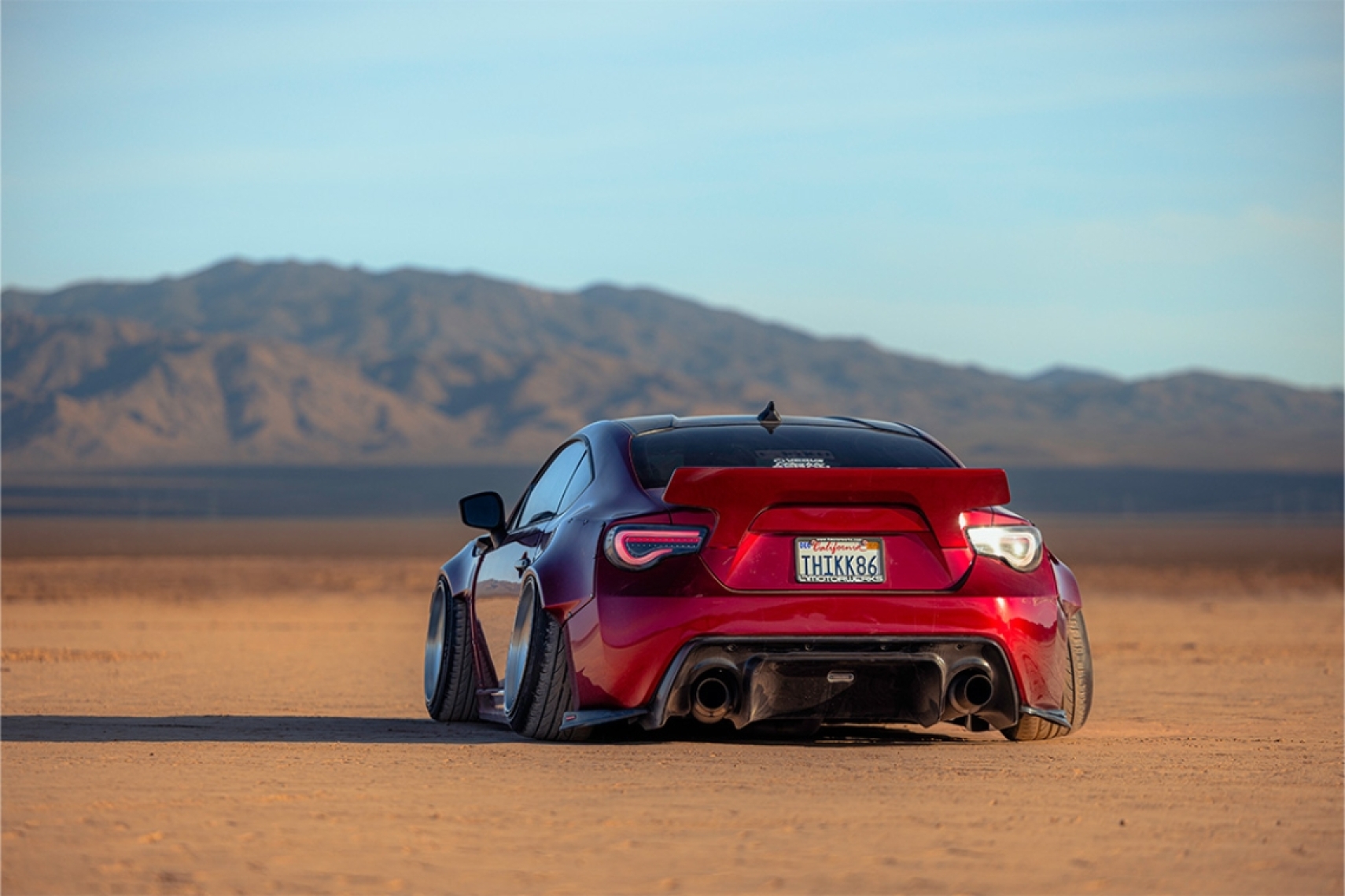 Rear view of Anthony Gonzales’ red widebody 2014 Scion FR-S parked in the desert with mountains in the background.
