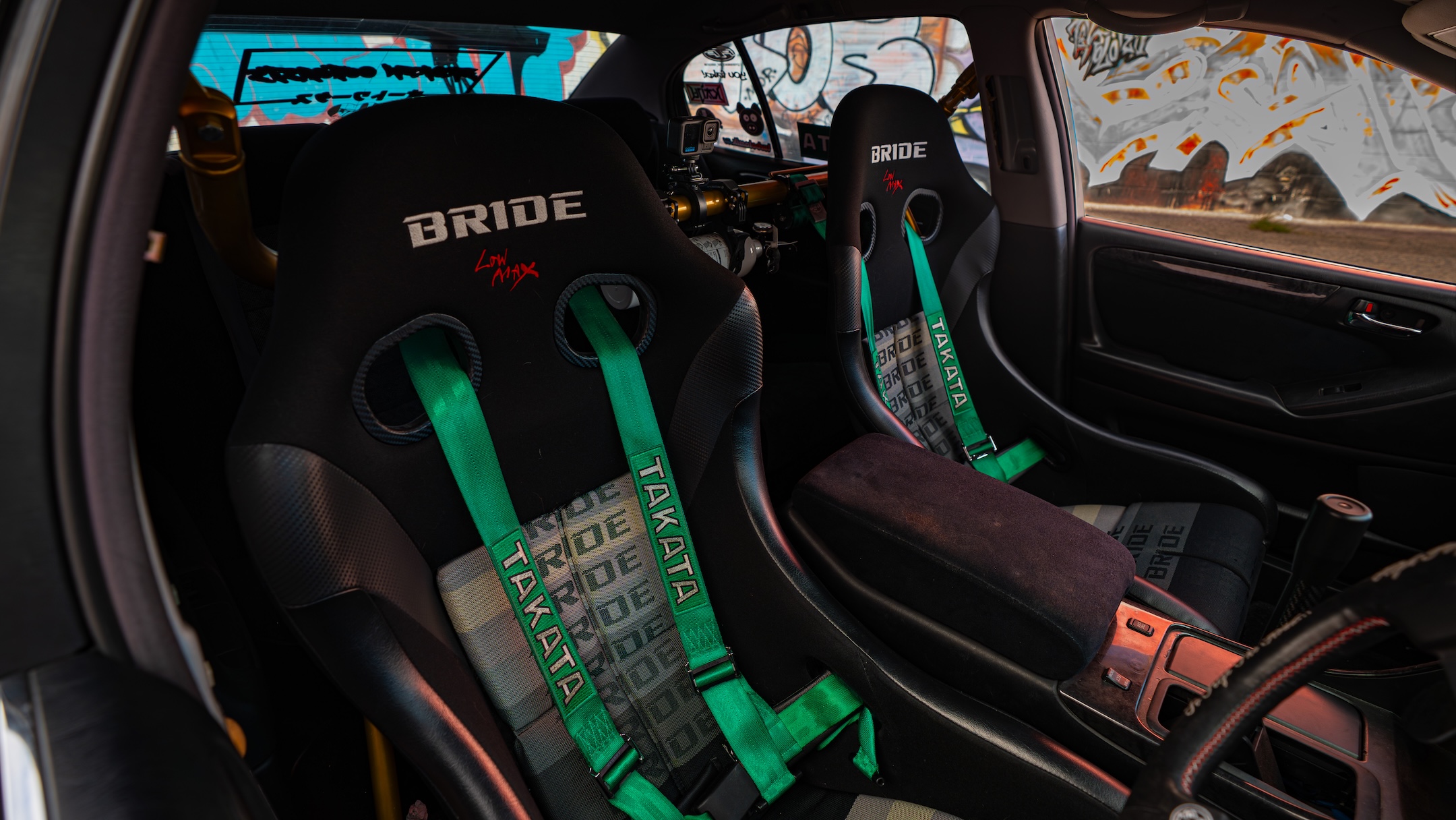 Interior view of Chris Burch’s 1997 Toyota Aristo showing the Bride front seats, Takata harnesses, center console, and street-focused cabin setup.