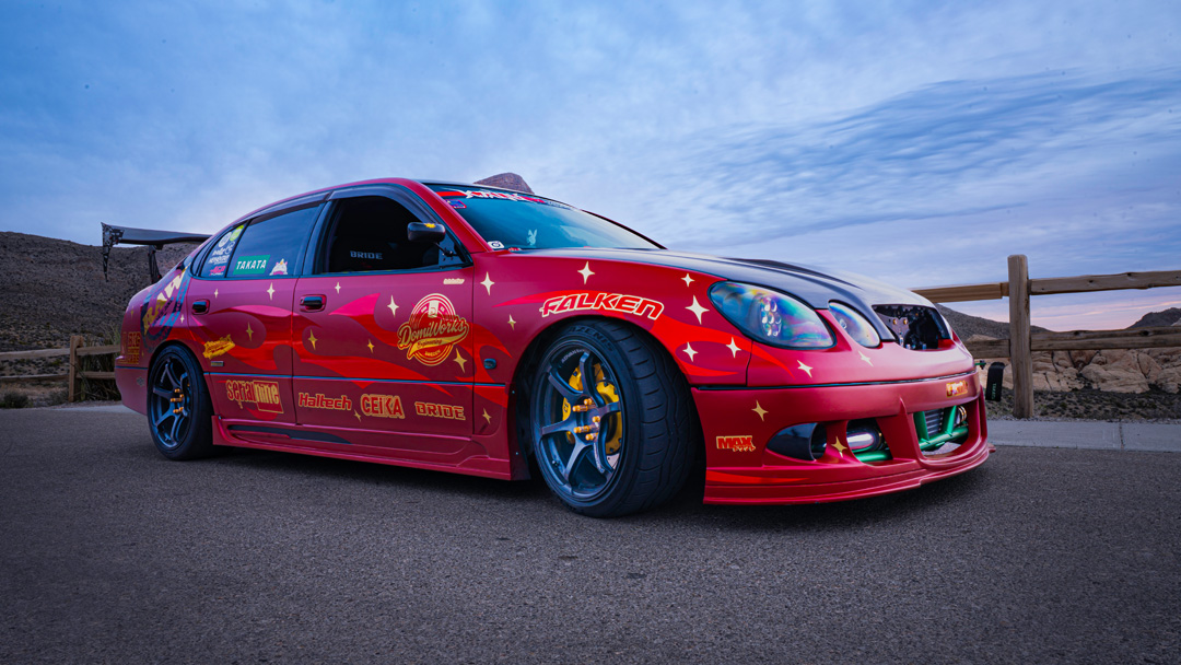 Chris Burch’s satin red 1997 Toyota Aristo with RAW livery, turbocharged 2JZ power, 8HP70 transmission swap, Advan RG4 wheels, Big Country Labs wing, and function-first street build details.