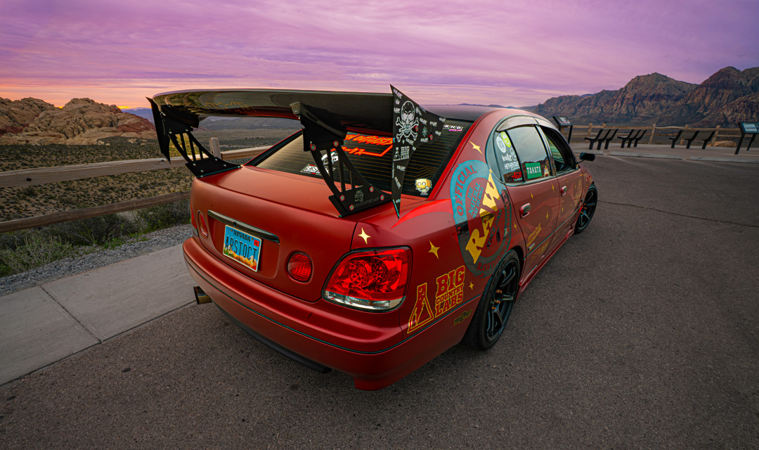 Chris Burch’s satin red 1997 Toyota Aristo with RAW livery, turbocharged 2JZ power, 8HP70 transmission swap, Advan RG4 wheels, Big Country Labs wing, and function-first street build details.