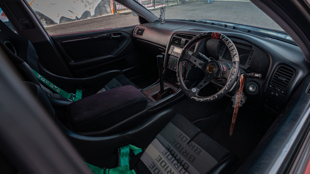 Chris Burch’s satin red 1997 Toyota Aristo with RAW livery, turbocharged 2JZ power, 8HP70 transmission swap, Advan RG4 wheels, Big Country Labs wing, and function-first street build details.