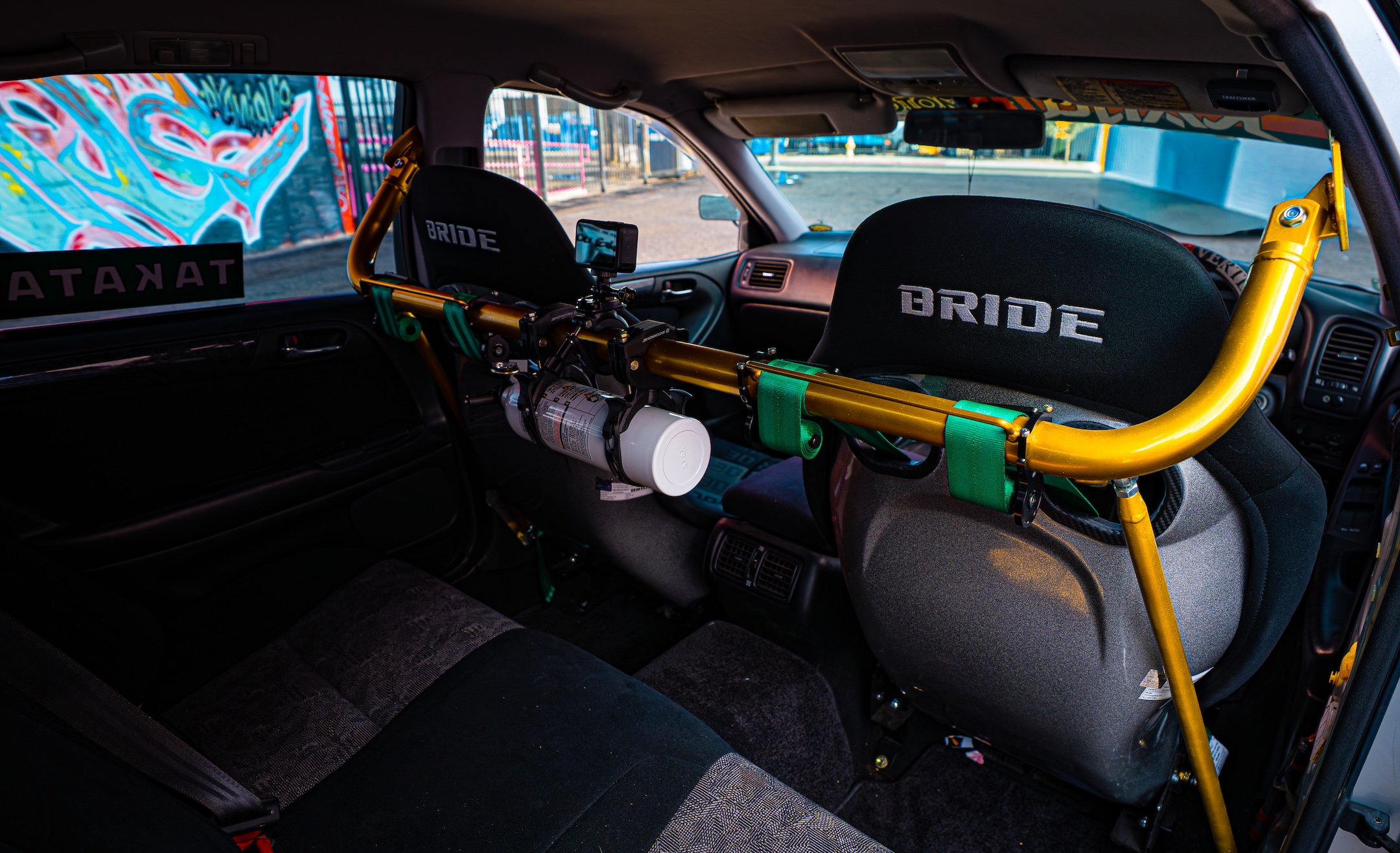 Rear interior detail of Chris Burch’s 1997 Toyota Aristo showing the Braum harness bar, mounted fire extinguisher, Bride seats, Takata harnesses, and in-car camera setup.