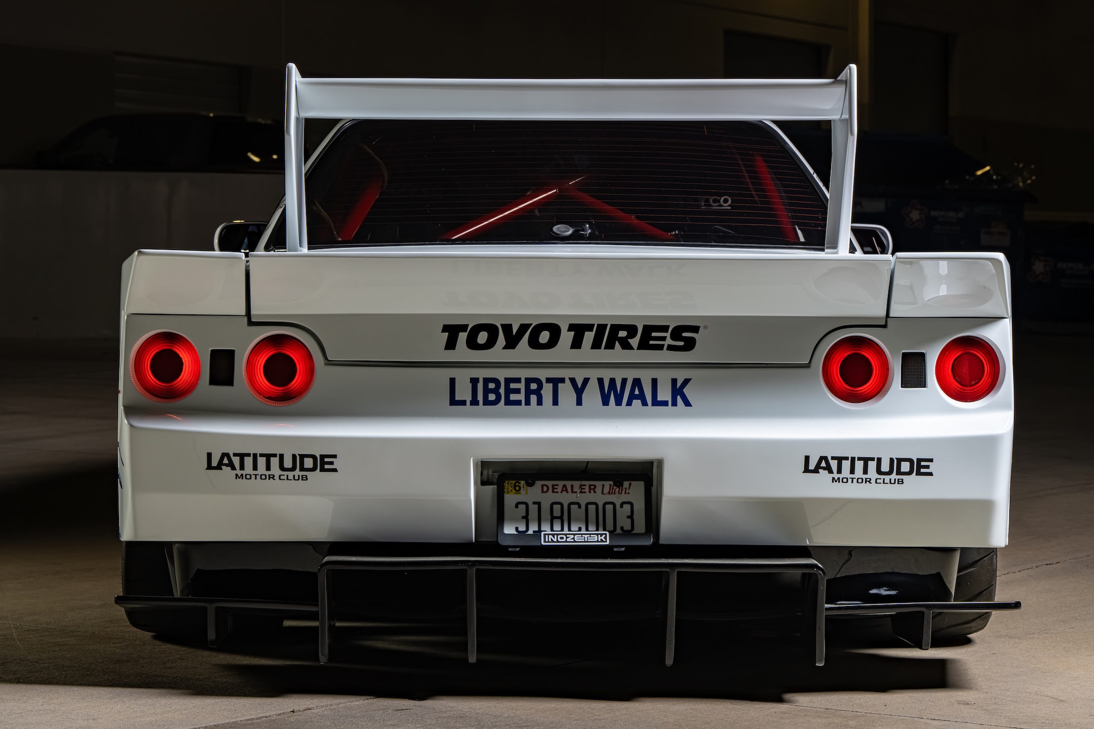Rear detail of Osmond Seangsuwan’s 1990 Nissan Skyline GT-R showing the Liberty Walk rear wing, Toyo Tires and Liberty Walk branding, illuminated tail lights, rear diffuser, and red Cusco roll cage.