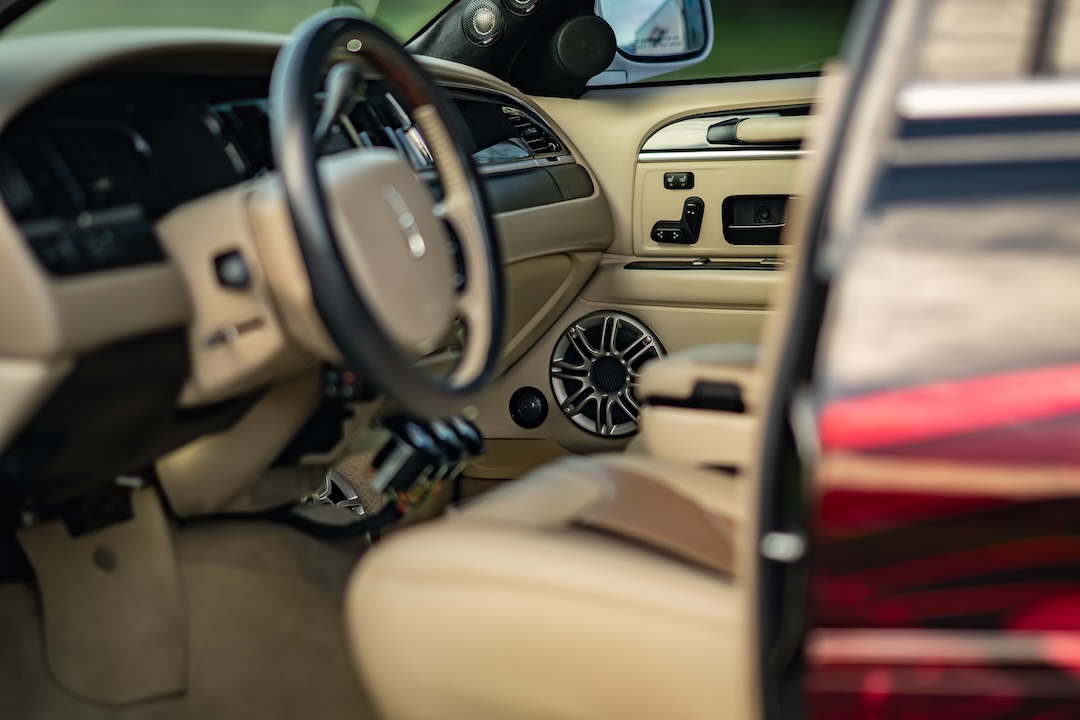 Interior detail of Sam Benischek’s 2006 Lincoln Town Car showing the custom two-tone cabin, steering wheel, door-mounted speaker pod, and reworked interior trim.