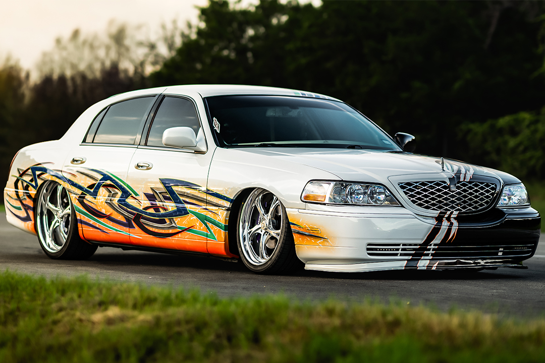 Front three-quarter view of Sam Benischek’s 2006 Lincoln Town Car showing the white side of the Two-Face custom graphic paint, low air suspension stance, KRNC forged wheels, chrome grille, and front lip.