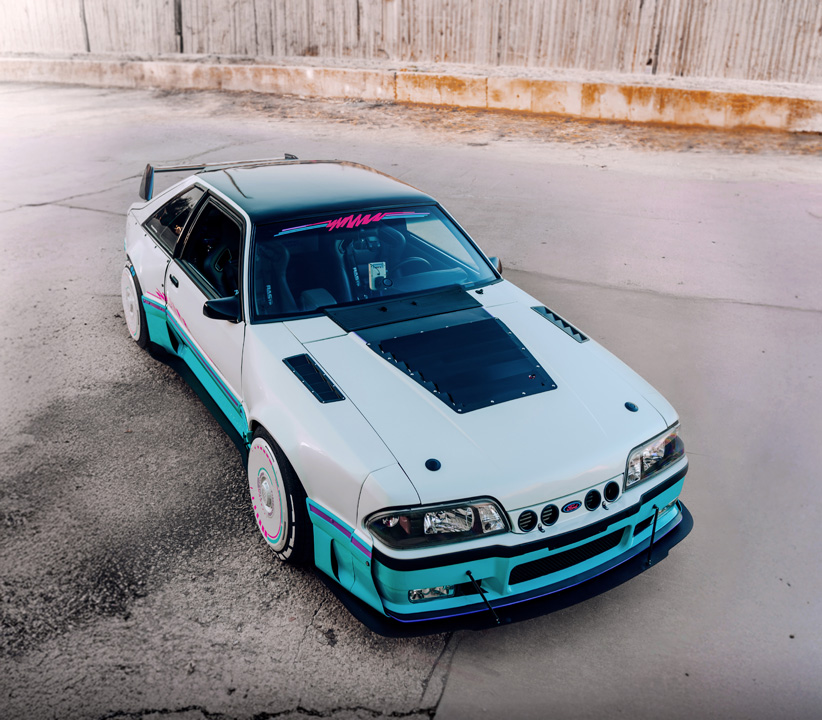 Regan McLaughlin’s 1988 Ford Mustang GT TimeFox with custom multi-tone paint, Ford Barra turbo swap, wide fiberglass fenders, retro Foxbody styling, HaloBLK wheel covers, custom interior, and nostalgic audio details.