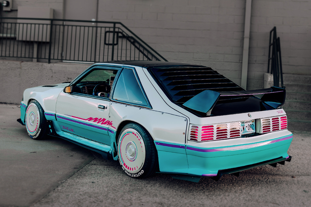 Rear three-quarter view of Regan McLaughlin’s 1988 Ford Mustang GT TimeFox showing the custom multi-tone paint, wide fiberglass fenders, rear window louvers, Evo-style rear wing, custom aero, and HaloBLK wheel covers.