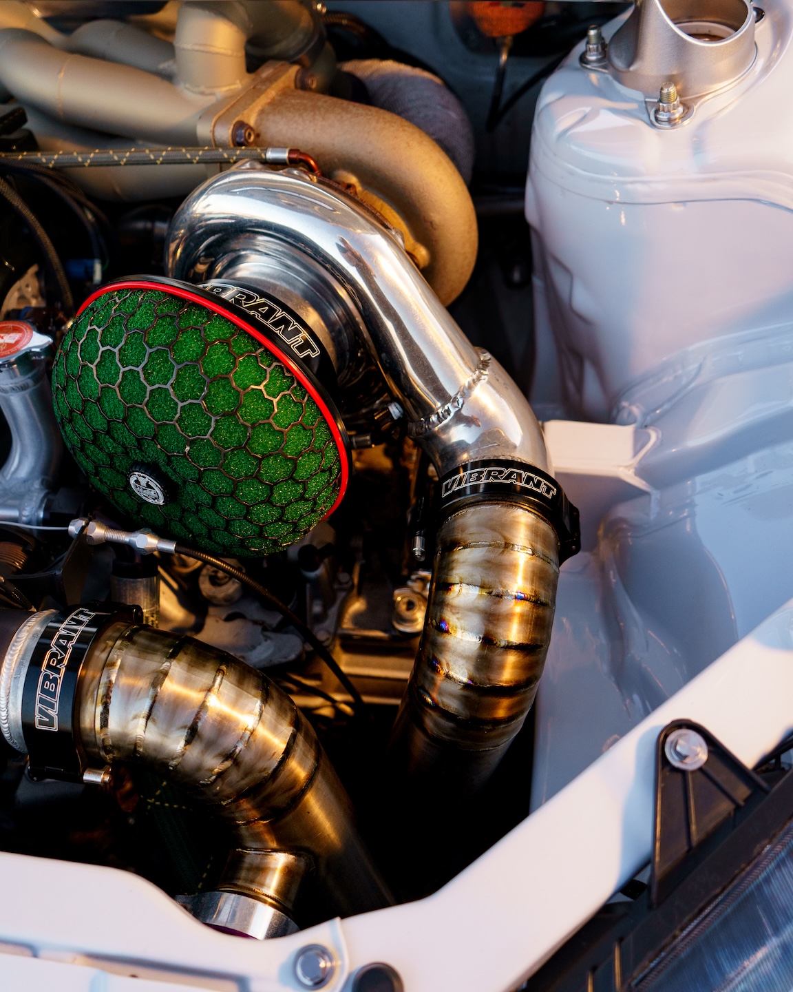 Close-up engine bay detail of Jonathan Ortiz’s 2005 Acura RSX Type-S showing the BorgWarner turbo, titanium charge piping, Vibrant Performance couplers, wrapped manifold, and tucked bay finish.