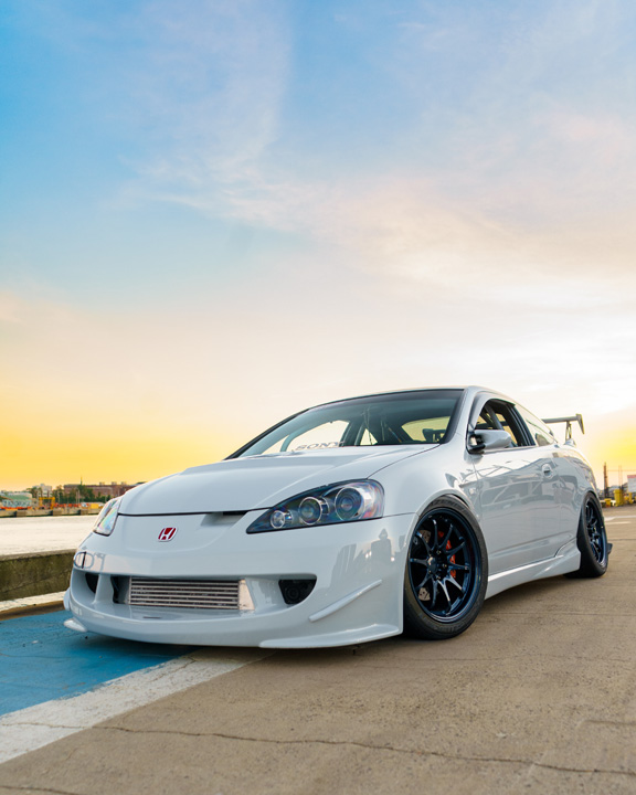 Jonathan Ortiz’s 2005 Acura RSX Type-S with Porsche PTS Fashion Grey paint, Mugen aero, J’s Racing details, blue Volk Racing CE28N wheels, turbocharged K-series engine bay, DC5R interior conversion, and Sony ES audio setup.
