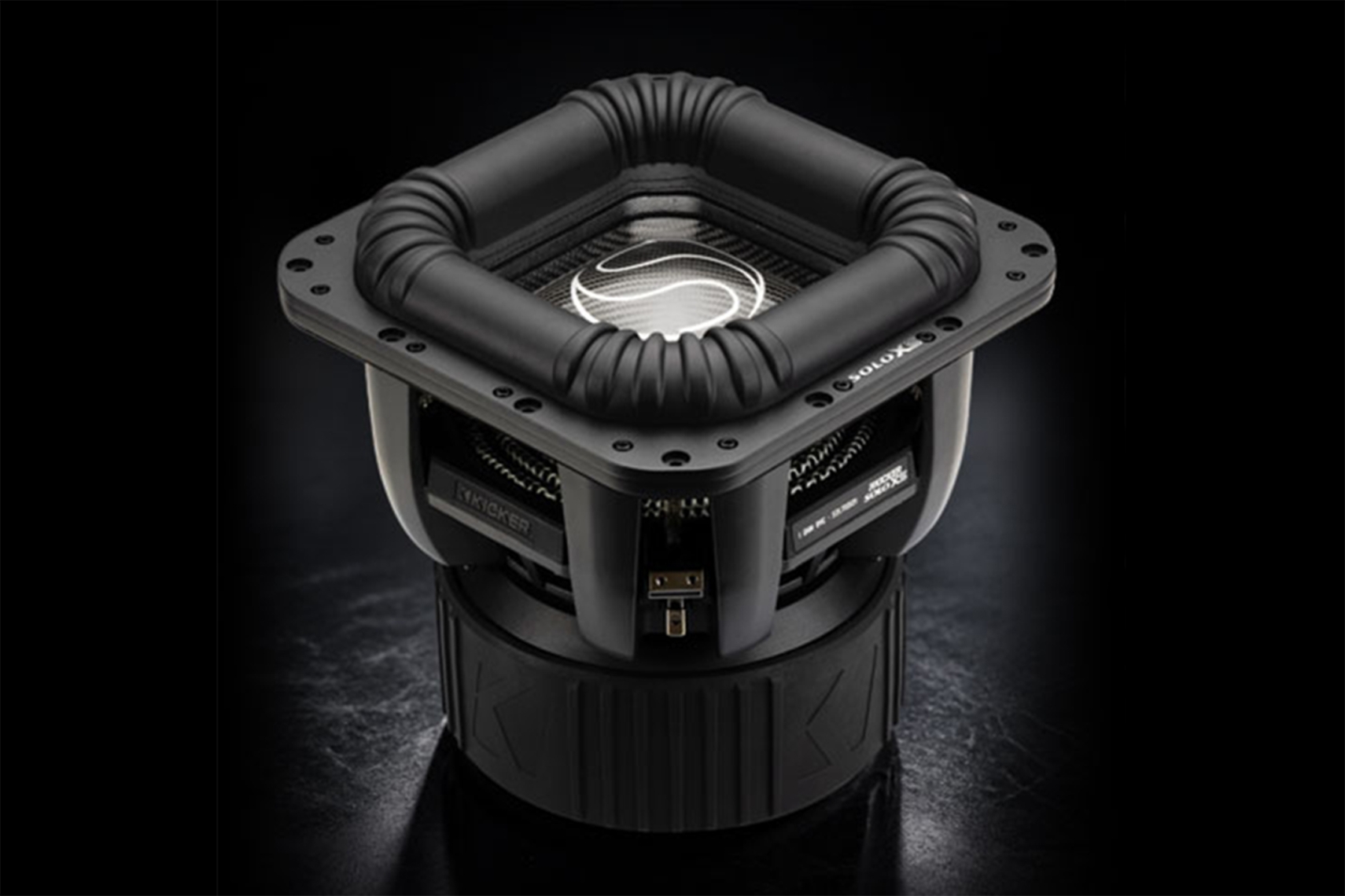 KICKER SoloXS L7XS square subwoofer shown from the front with large NBR surround, carbon-look cone, and oversized motor assembly.