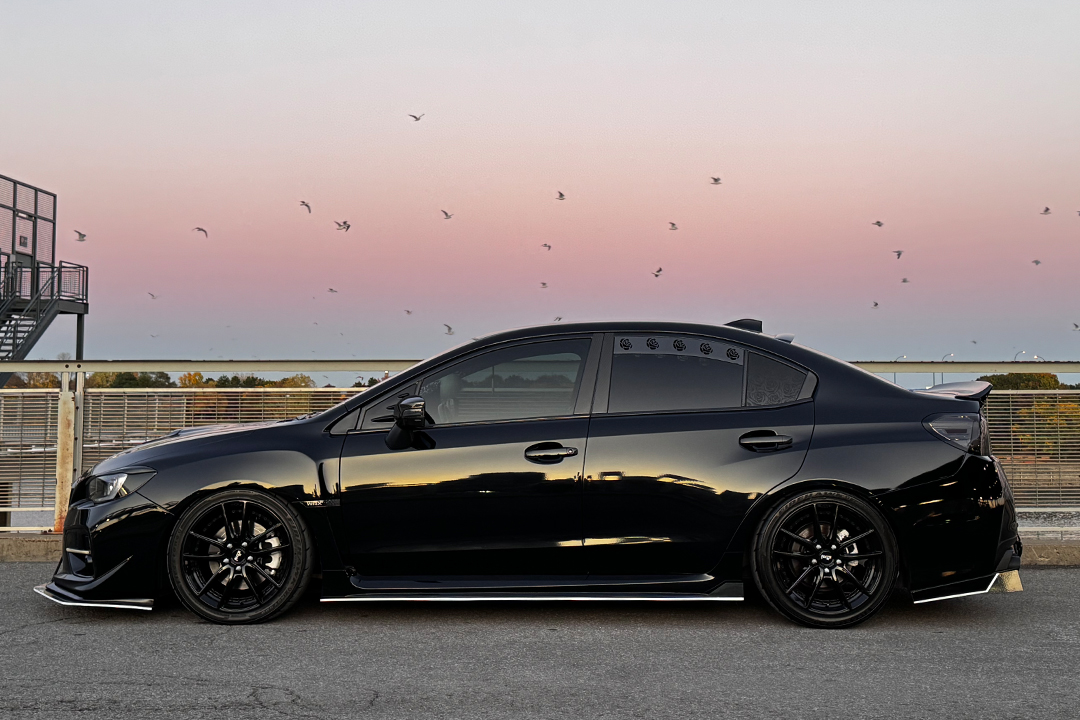 Side profile of Melissa Pelletier’s black 2017 Subaru WRX showing its lowered stance, gloss black Niche wheels, ADE Creations side skirts, and black-and-white exterior theme.
