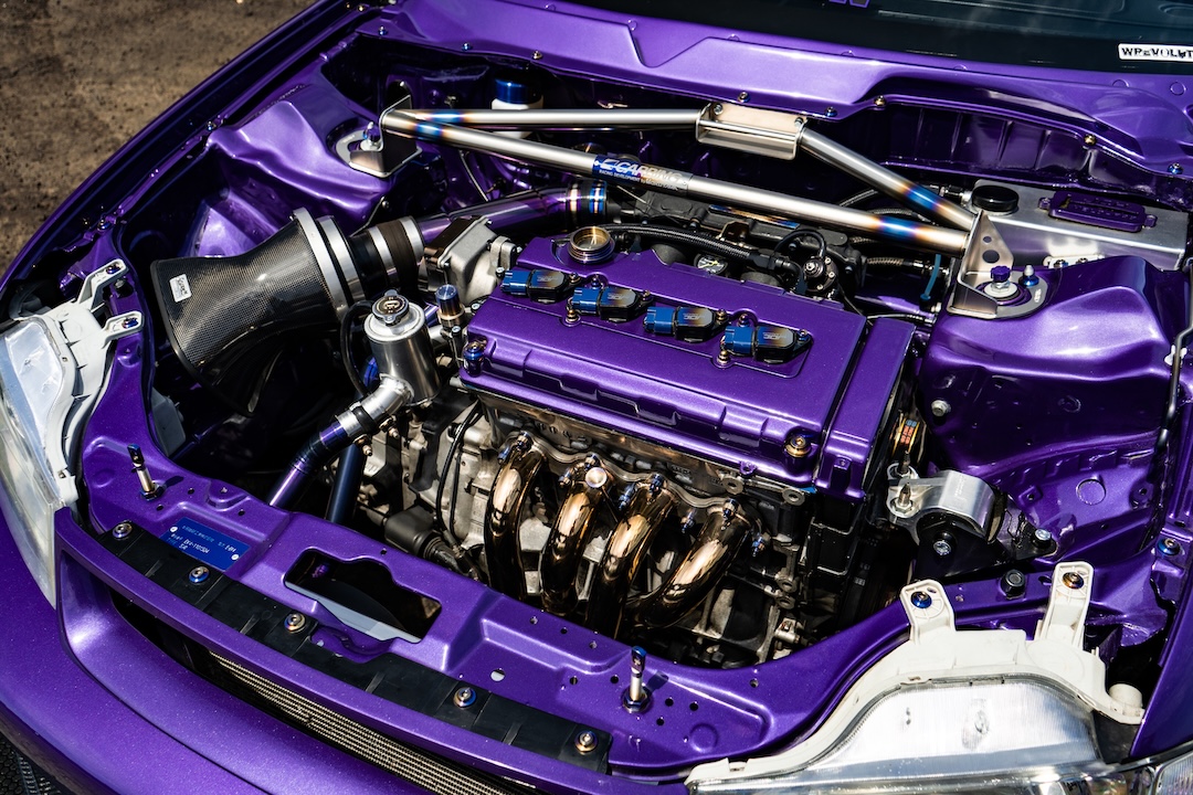 Engine bay of Brandon Elste’s 1996 Honda Civic showing its B16A2 engine swap, custom titanium intake components, Skunk2 Alpha header, and tucked engine bay.