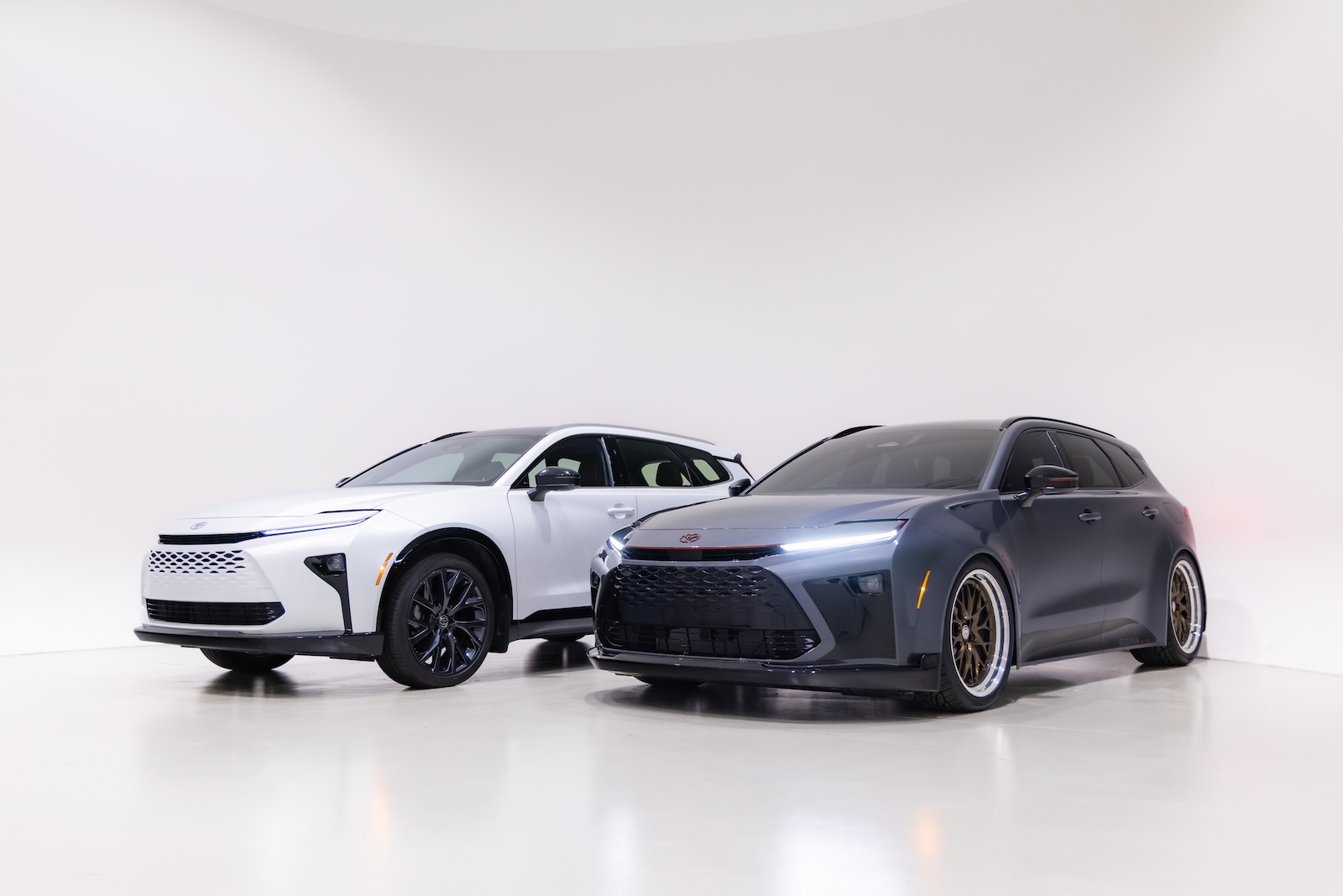 Front three-quarter comparison of the Toyota Crown Signia GT-S Concept in dark gray metallic alongside a white production Crown Signia, highlighting the concept's lowered stance, widebody styling and 21-inch HRE wheels.